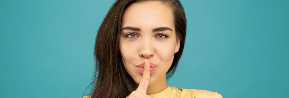 a photo of a girl in a yellow shirt doing the shh sign