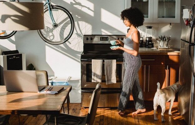 A woman with a hot drink in the kitchen next to a dog
